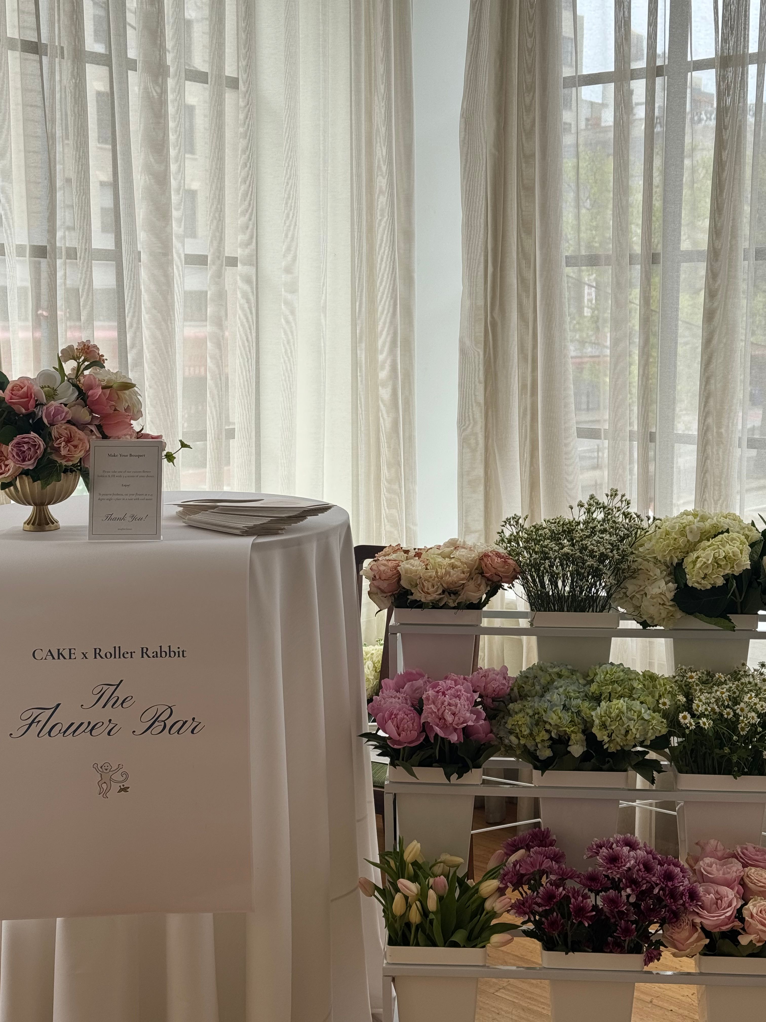 CAKE x Roller Rabbit flower bar with pink roses, peonies, hydrangeas, tulips, and daisies arranged for guests to build bouquets.